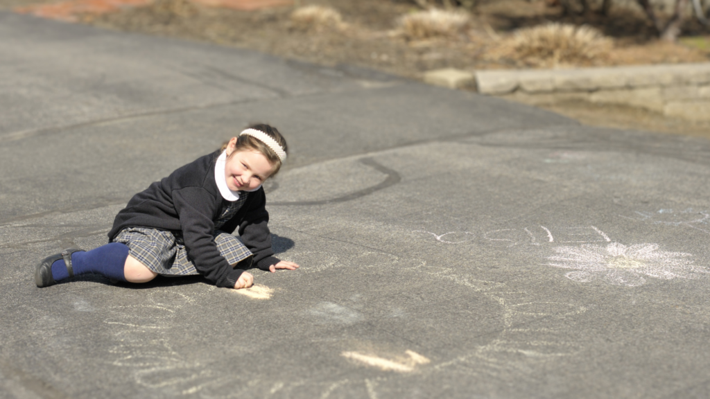 Young female child in school uniform drawing on pavement with chalk